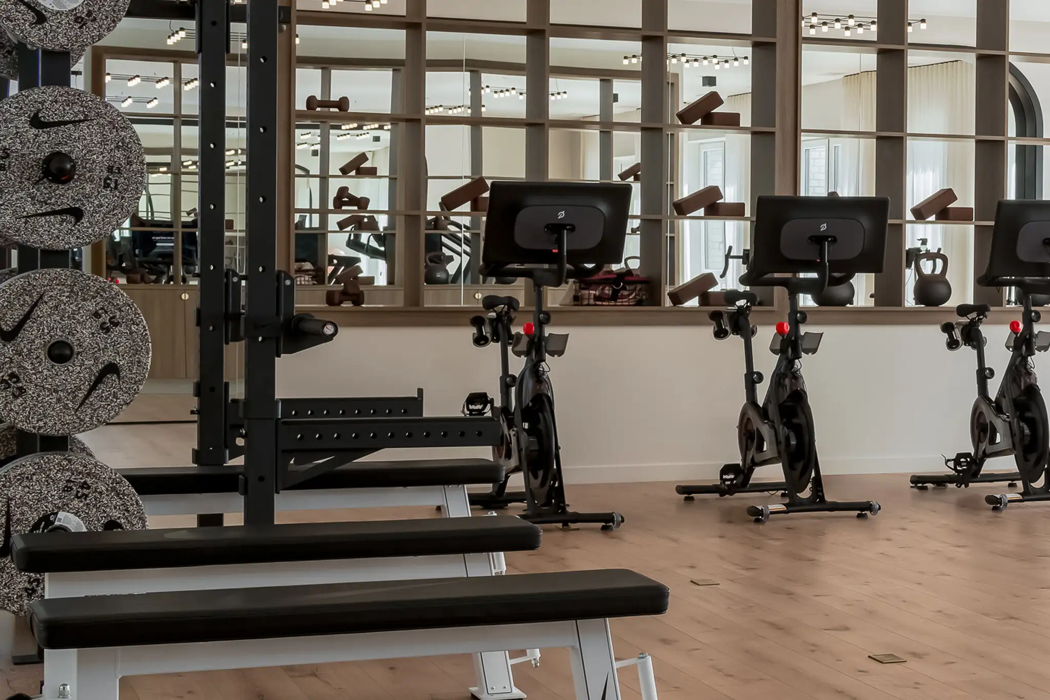 Strength rack and benches in front of Peloton bikes and a mirror wall